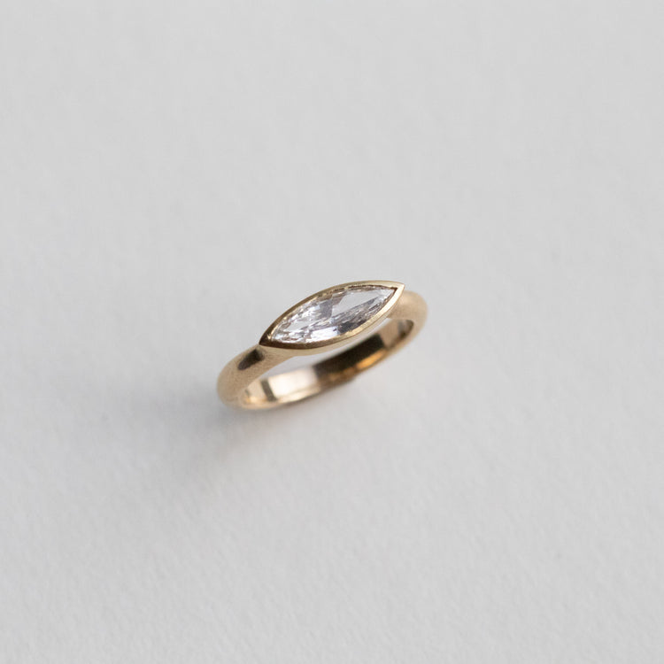 “Elegant 18ct yellow gold ring set with a marquise-cut diamond in a minimalist bezel, paper shot perspective view