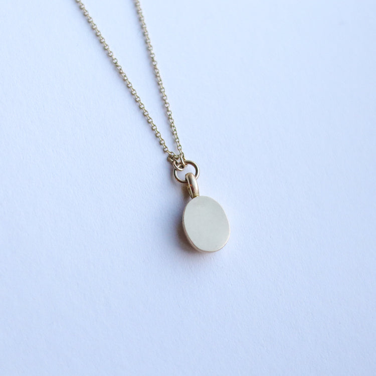 Close up of solid 9ct yellow gold oval pendant necklace with pave champagne diamond details and a flush set brown oval natural diamond. On a loop in-line on a fine chain. photographed on paper, view of the back.