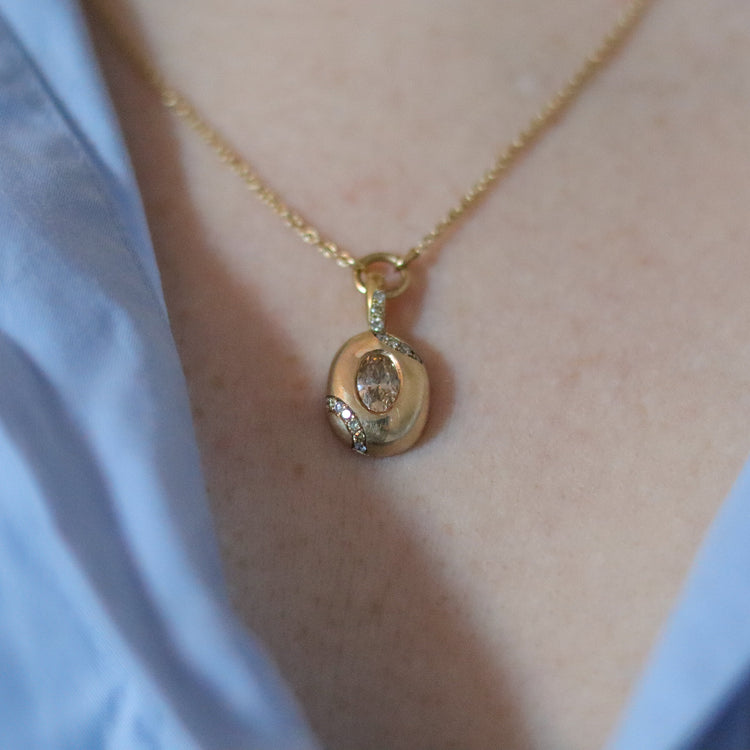 goldfinch jewellery Close up of solid 9ct yellow gold oval pendant necklace with pave champagne diamond details and a flush set brown oval natural diamond. On a loop in-line on a fine chain. Photographed on model.