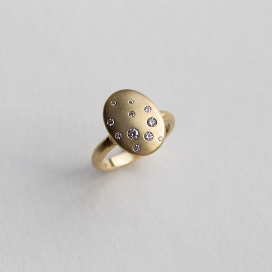 goldfinch jewellery Contemporary 18ct yellow gold oval disc ring with scattered diamond detailing, shown at angle on paper