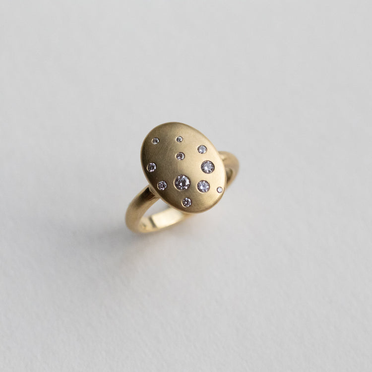 goldfinch jewellery Contemporary 18ct yellow gold oval disc ring with scattered diamond detailing, shown at angle on paper