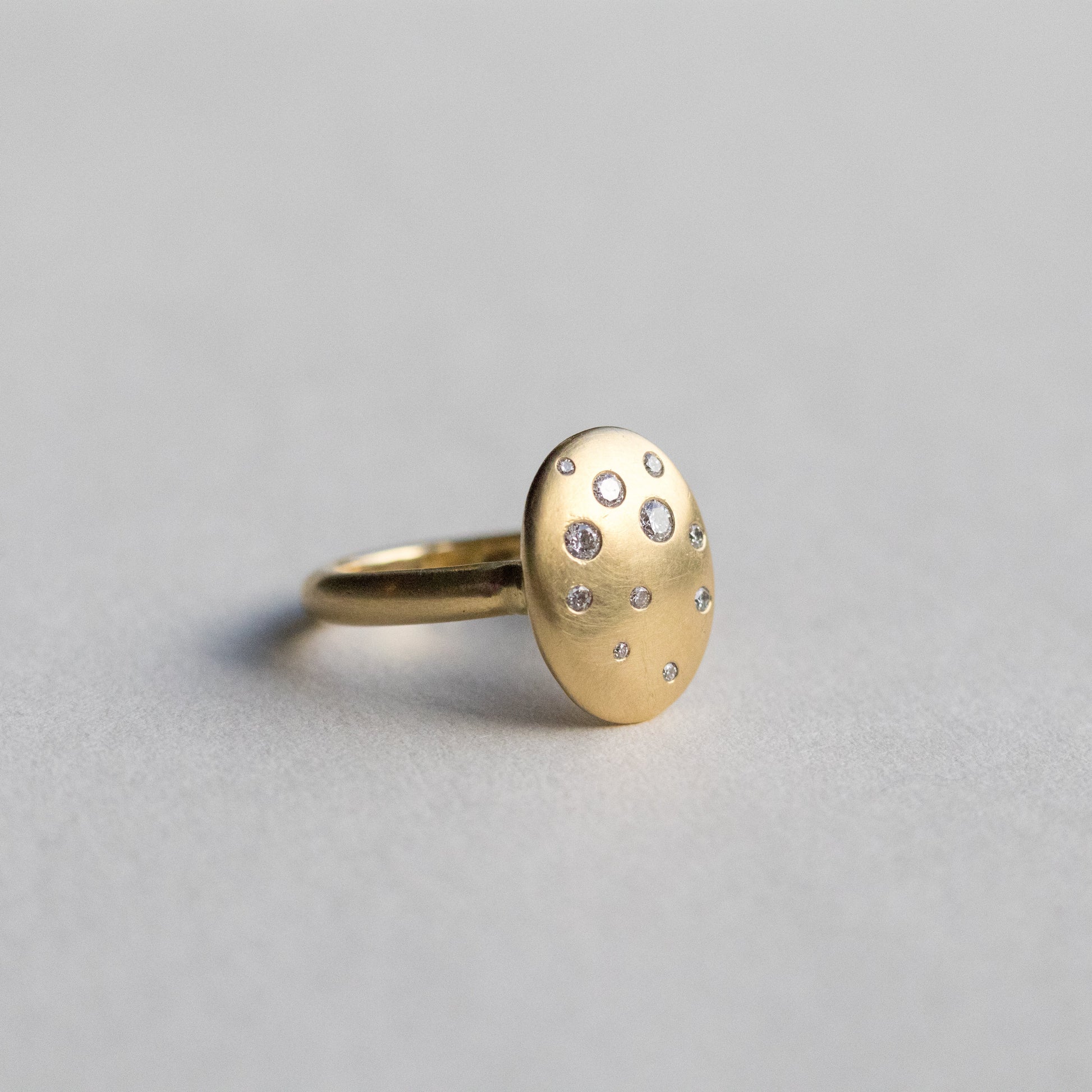 Contemporary 18ct yellow gold oval disc ring with scattered diamond detailing, shown at angle on paper 