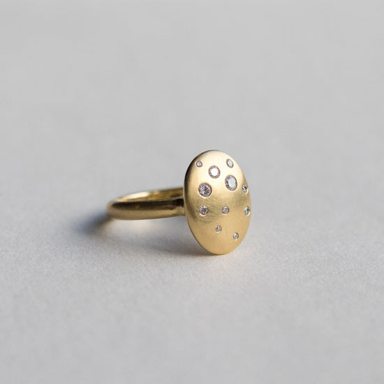 Contemporary 18ct yellow gold oval disc ring with scattered diamond detailing, shown at angle on paper 