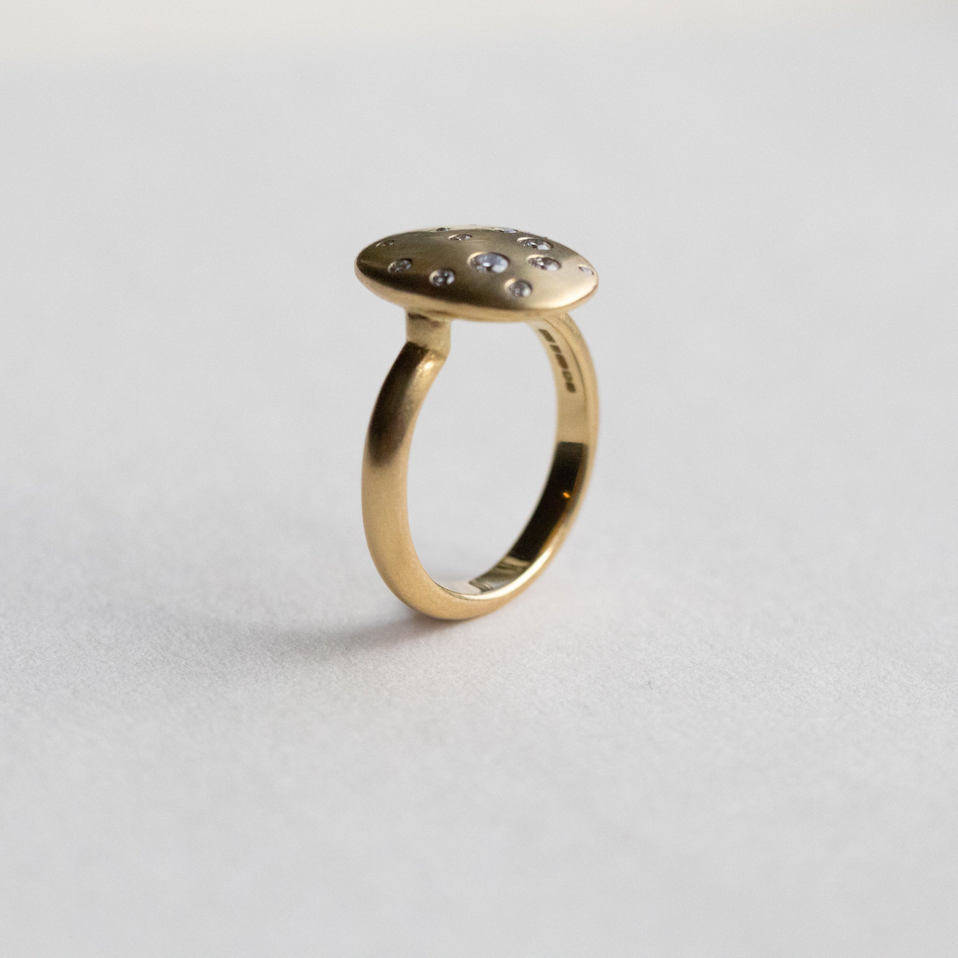 Contemporary 18ct yellow gold oval disc ring with scattered diamond detailing, shown is side view on paper
