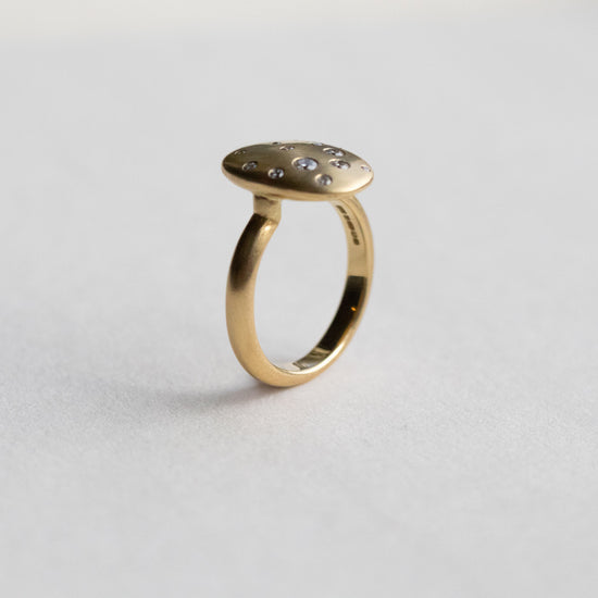 Contemporary 18ct yellow gold oval disc ring with scattered diamond detailing, shown is side view on paper